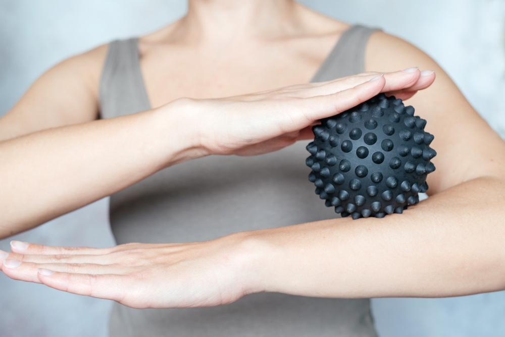 A woman holds a spiky trigger point massage ball used for muscle pain relief