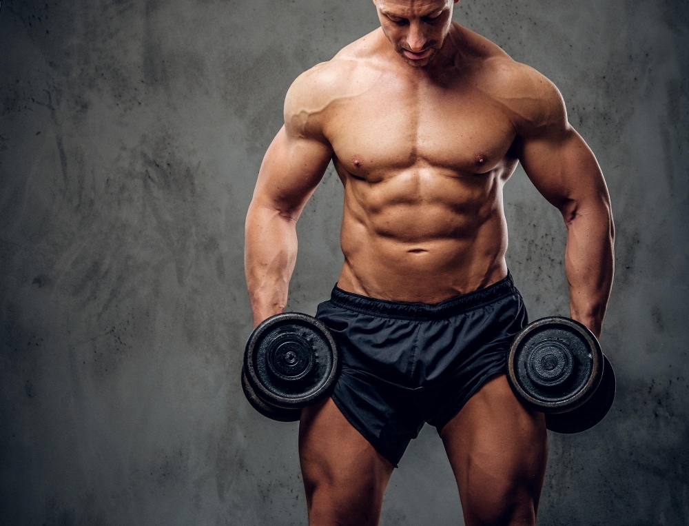 Attractive muscular bodybuilder is doing exercises with barbels and showing his muscules on the dark background.