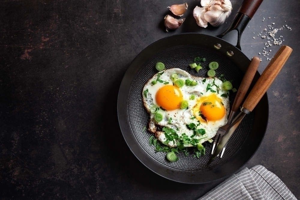 Fried eggs with vegetables on pan