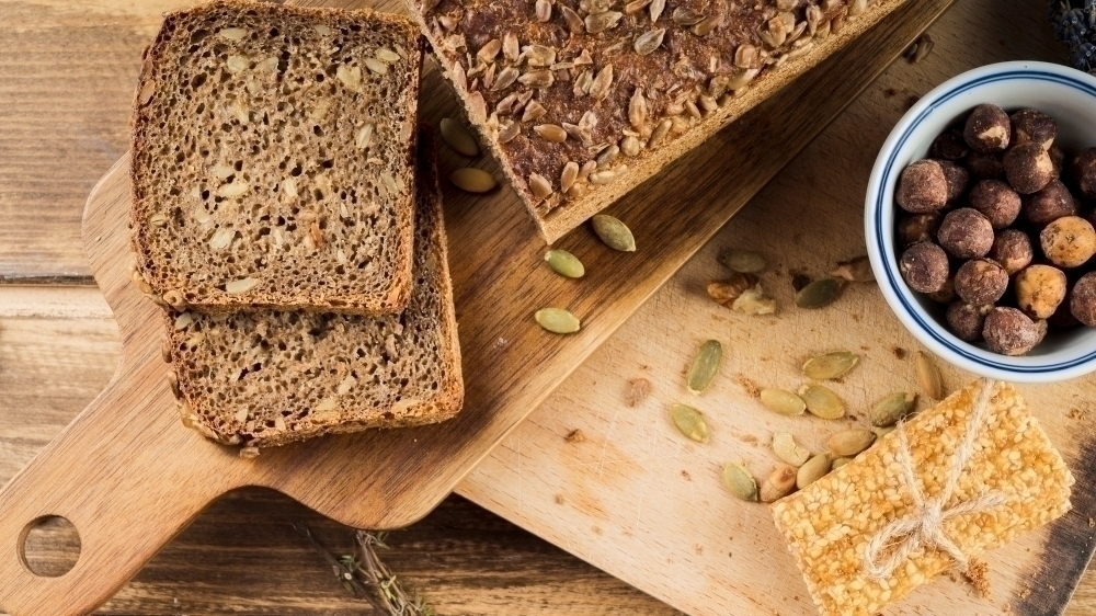 Healthy sunflower seed bread and hazelnut bowl with protein bar on chopping board2