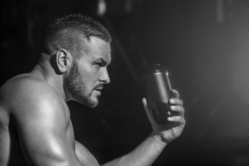 Lifestyle portrait of handsome muscular man drinking water in the gym Muscular man drinking water Holding bottle water Black and white