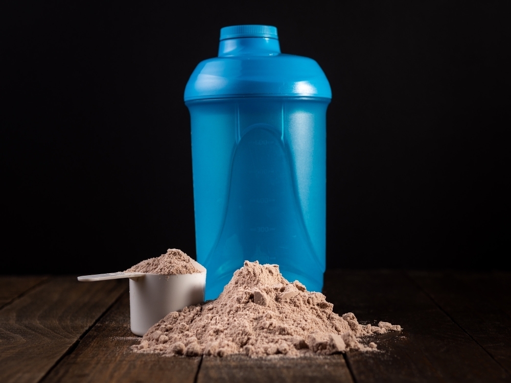 Measuring scoop of whey protein on wooden table to prepare a milkshake.