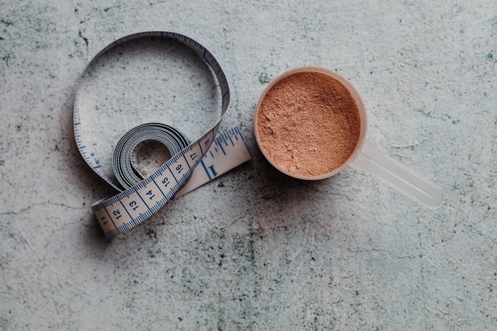 Scoop or spoon of whey protein with visible texture. Chocolate flavor. Concrete background
