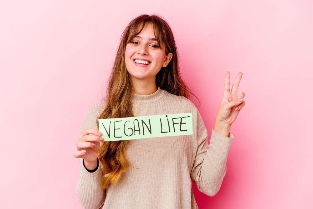 Young caucasian woman holding a vegan life placard isolated showing number two with fingers.