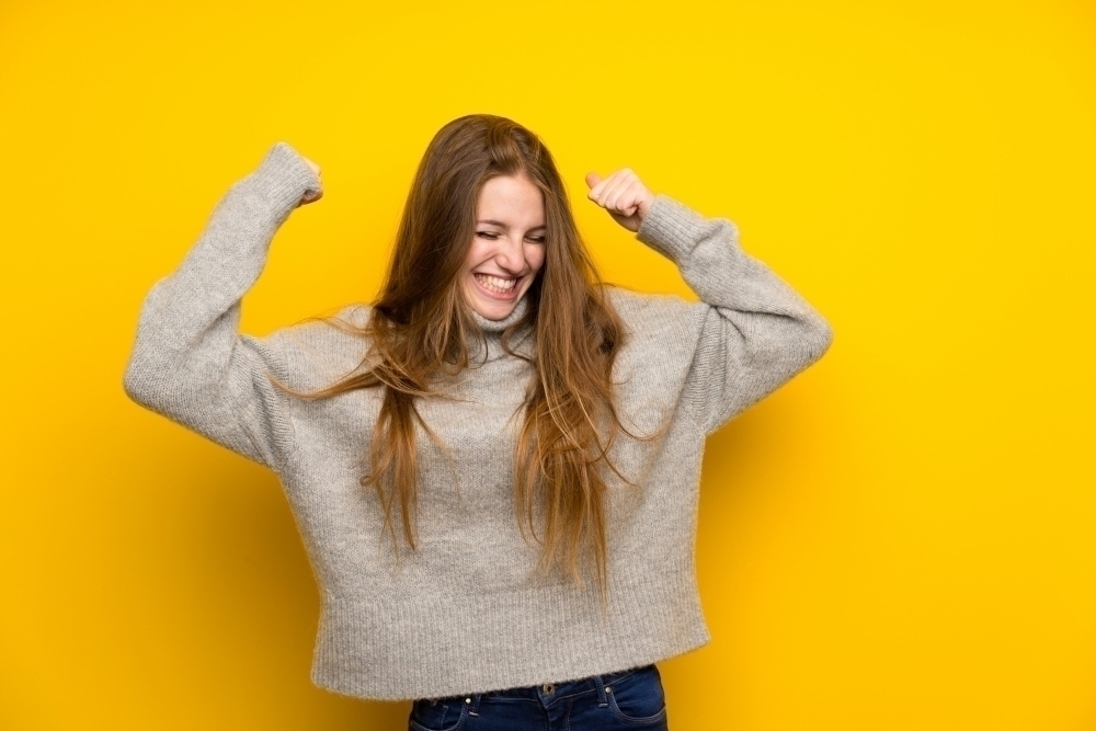 Young woman with long hair over yellow celebrating a victory