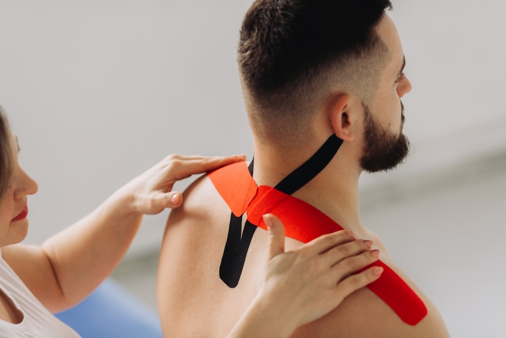 physiotherapist applying red black kinesio tapes patients back his office