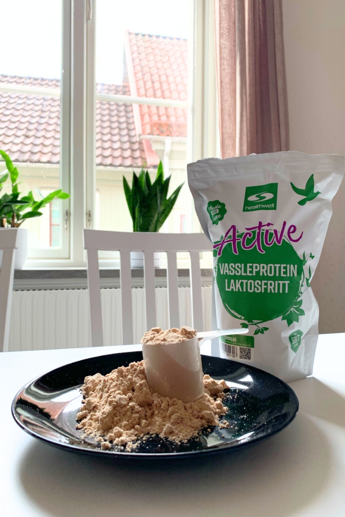 Skopa med chokladpulver på tallrik framför påsen Healthwell Active Vassleprotein Laktosfri tagen av oss