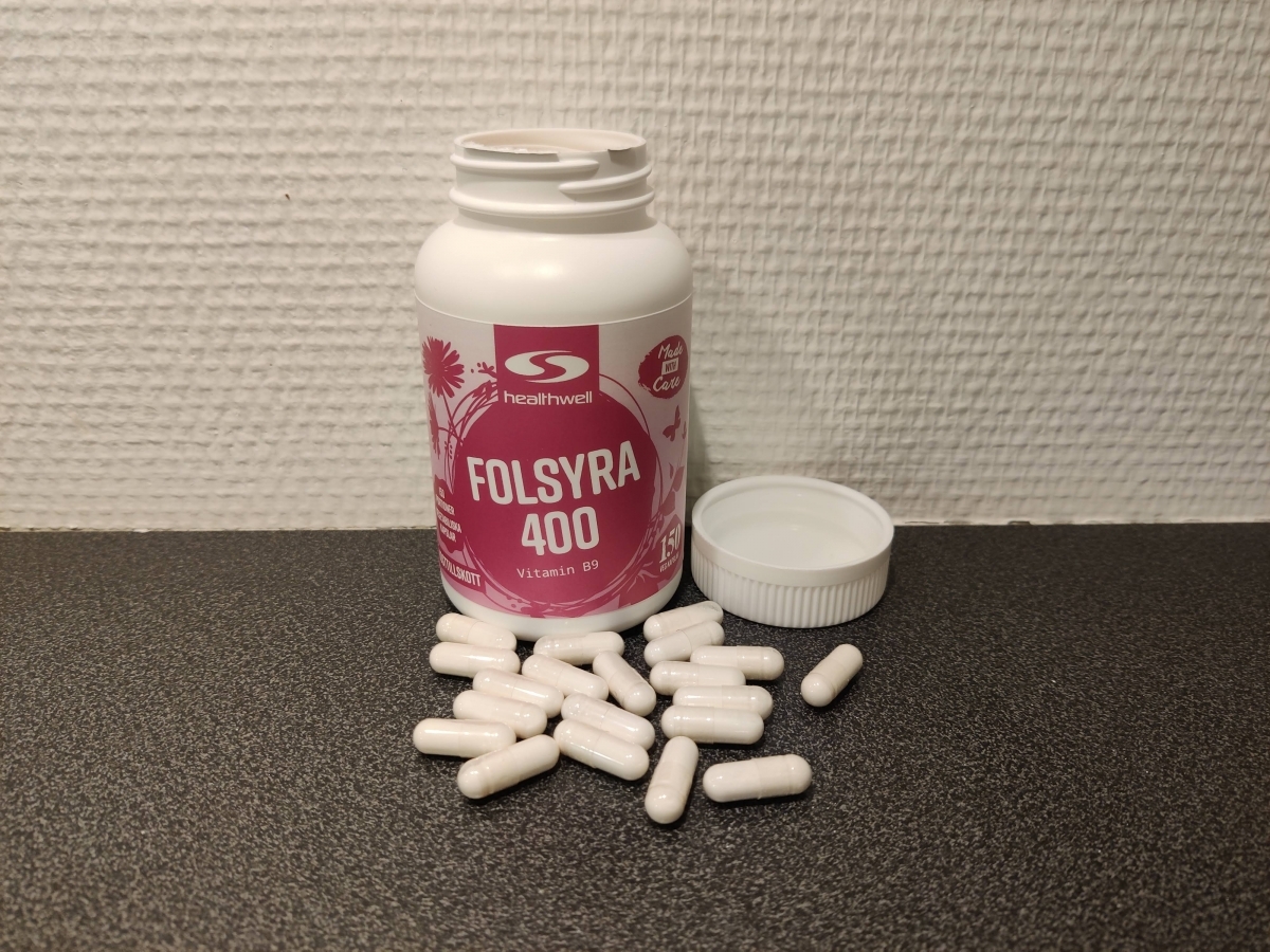 Öppen burk av Healthwell Folsyra 400 med kapslar utspridda på bänken, foto taget av oss under testet