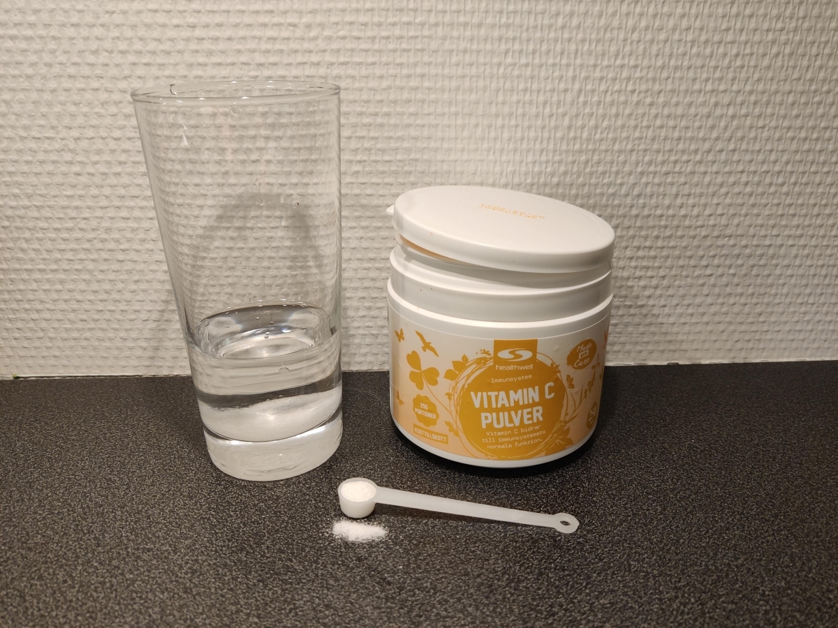 Healthwell Vitamin C Pulver med skopa och glas vatten, fotad av oss under testet