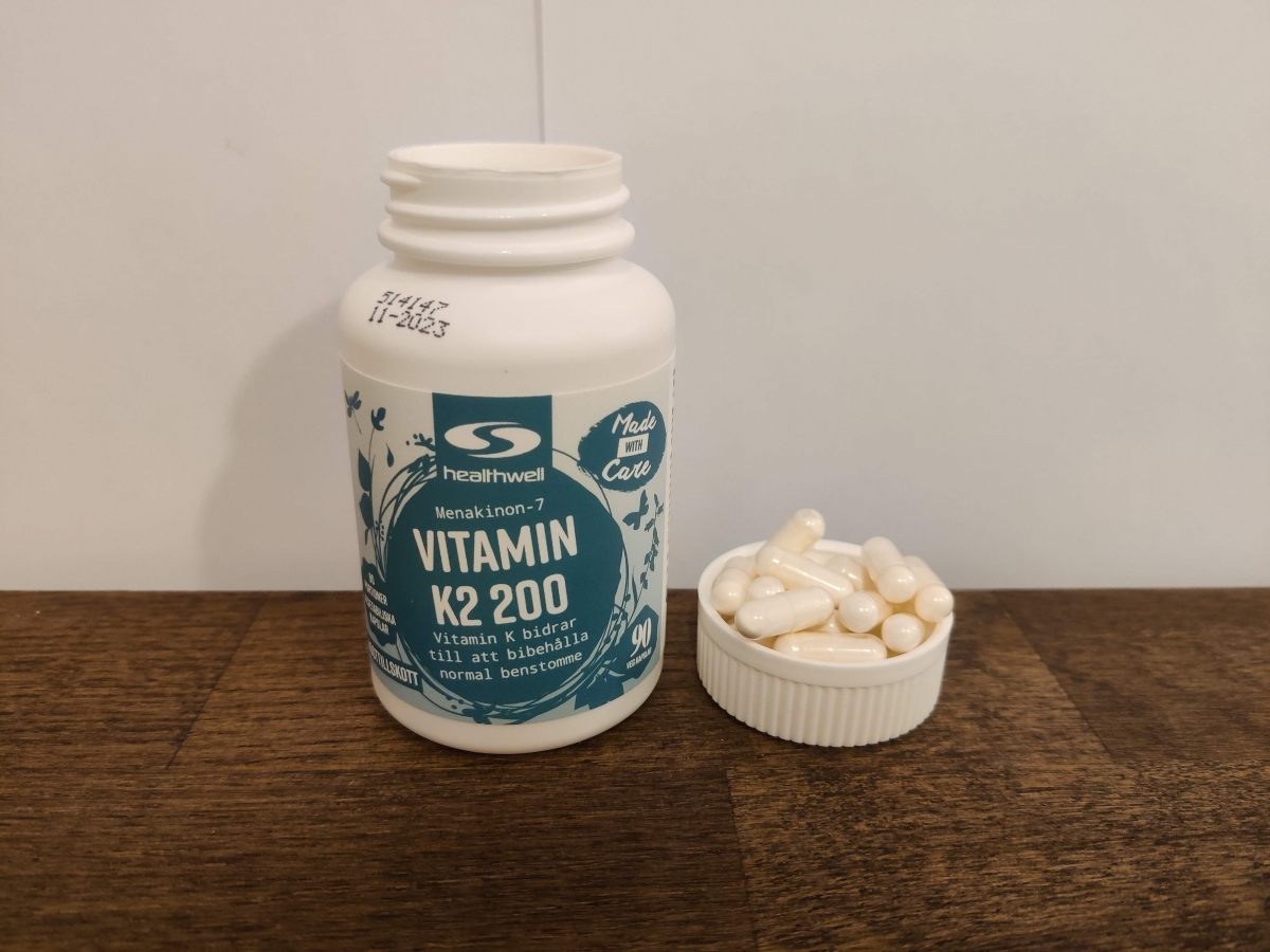 Healthwell Vitamin K2 på träbord, kapslar samlade intill locket, fotograferad av oss
