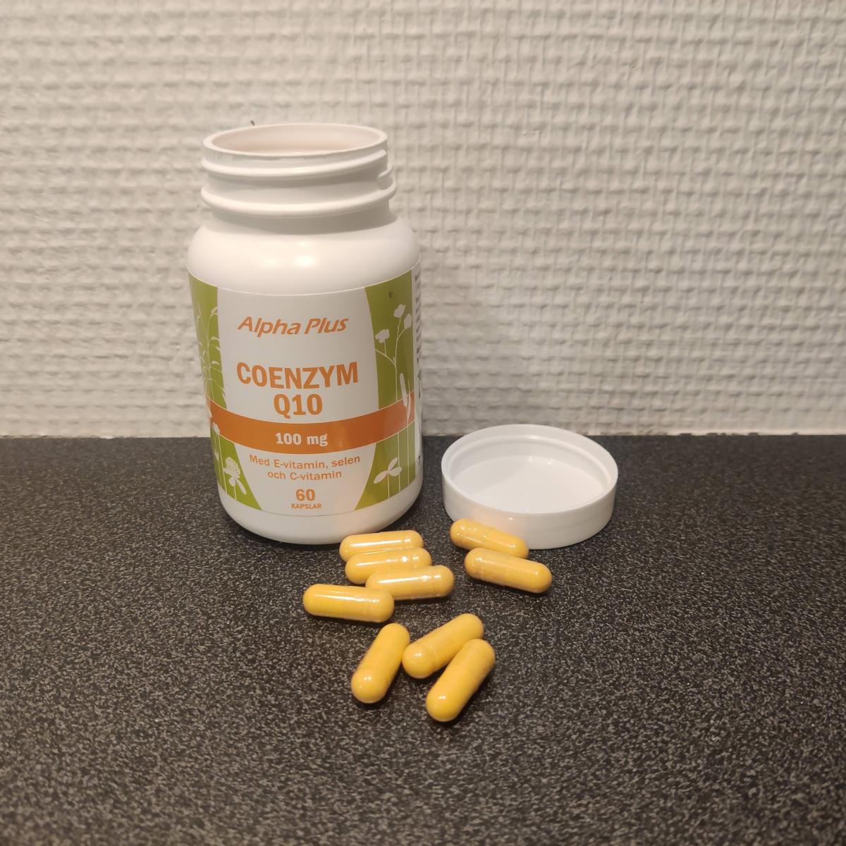 Alpha Plus Coenzym Q10 på träbord med kapslar bredvid, taget av oss