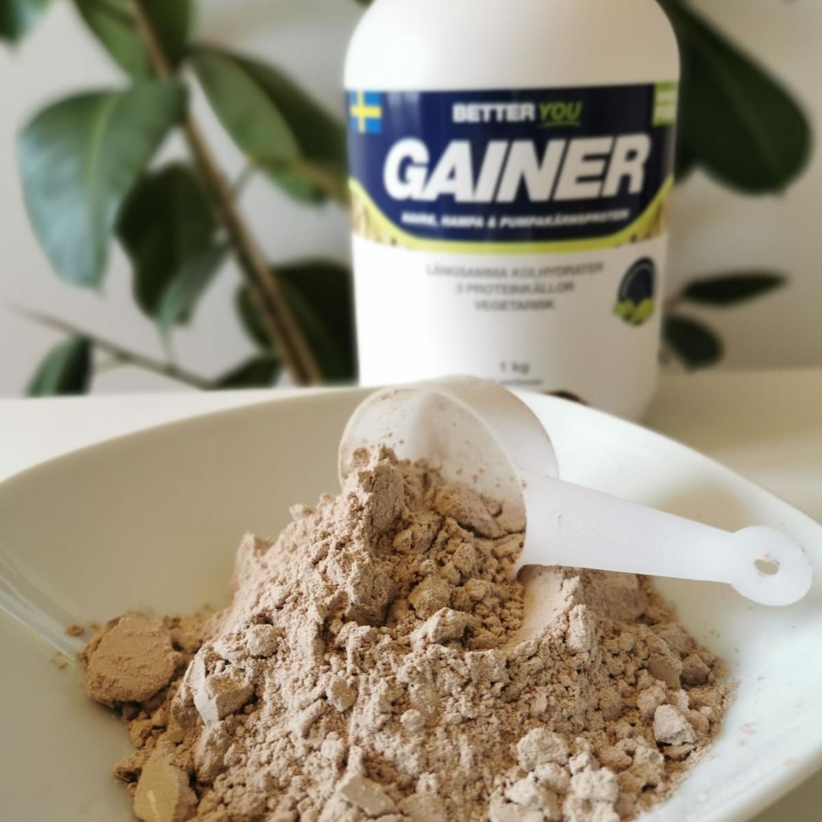 Pulver i skål med skopa framför burken Better You Vegetarisk Gainer fotad i dagsljus
