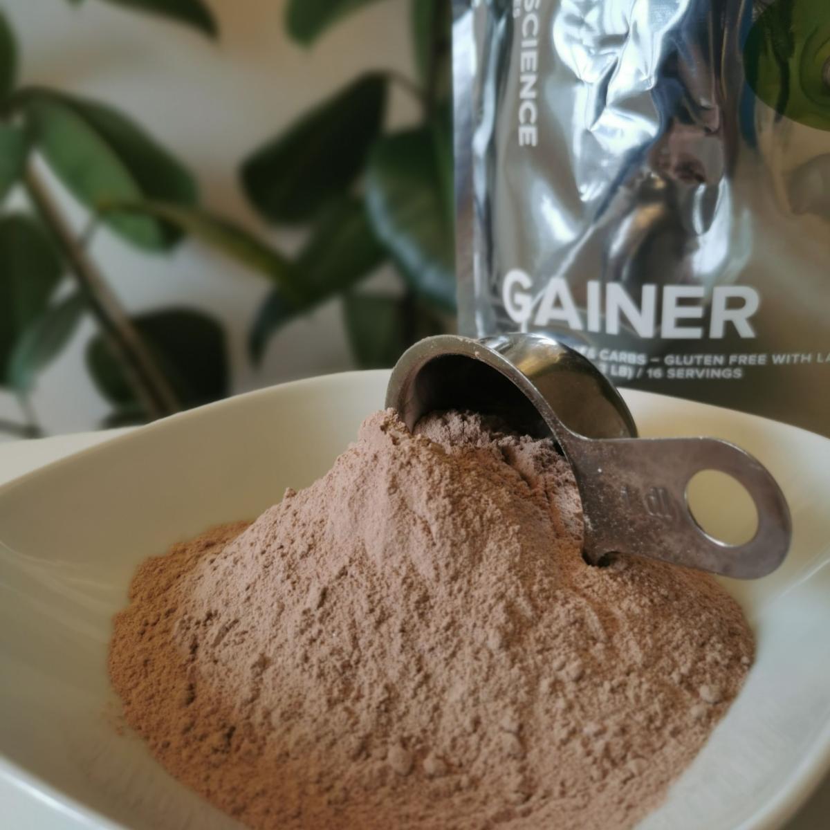 Chokladsmakad gainer som pulver i skål med metallskopa foto av oss