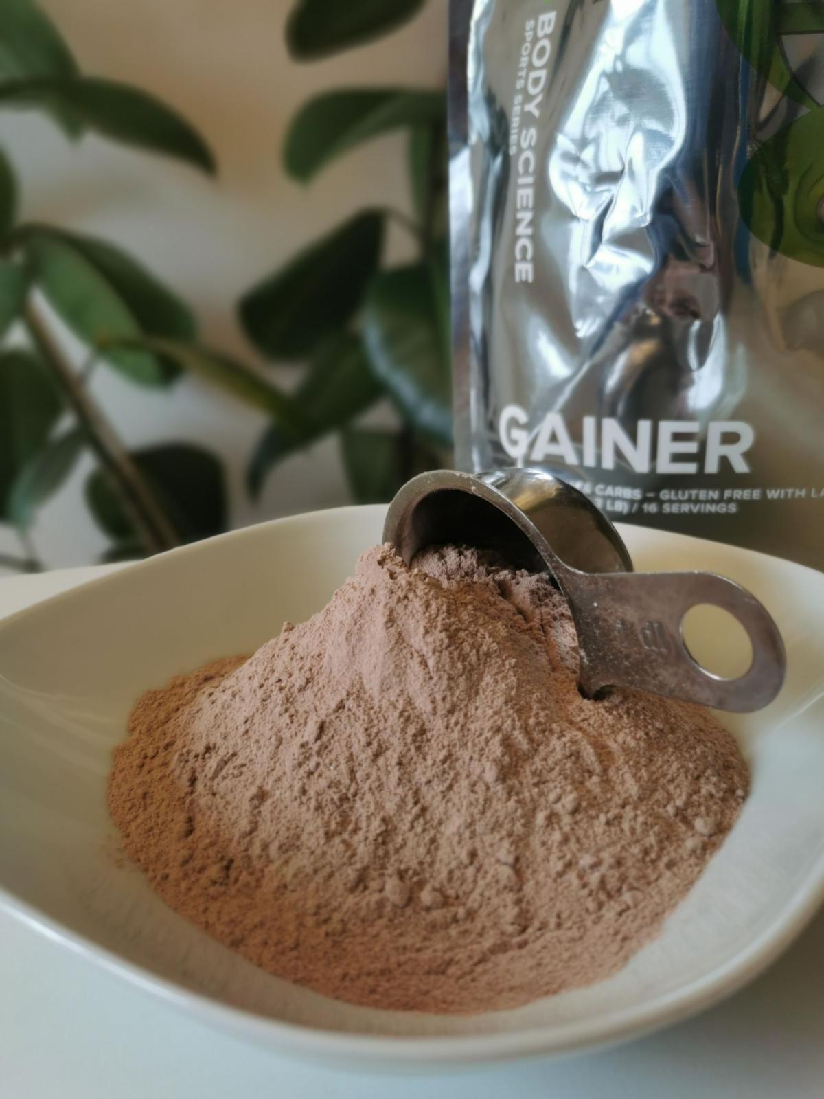 Chokladsmakad gainer som pulver i skål med metallskopa foto av oss