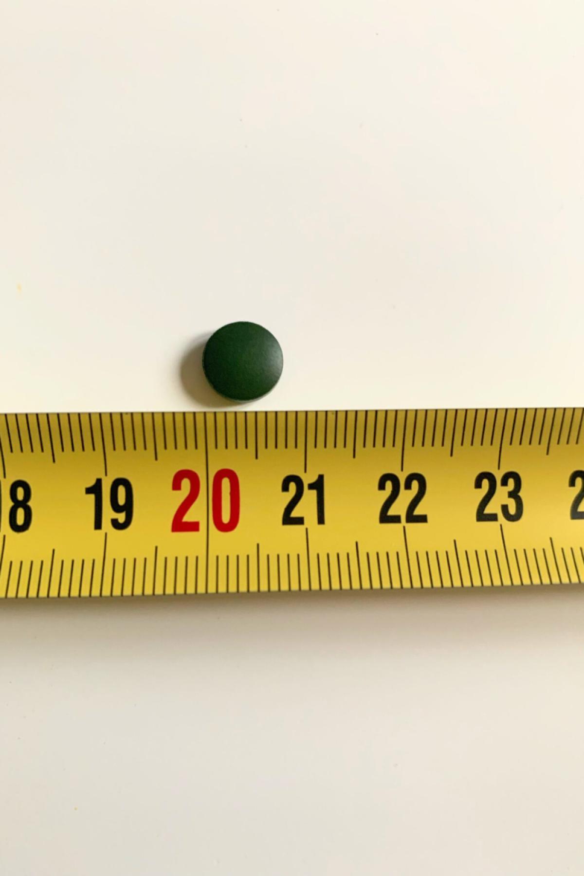 Mörkgrön chlorella-tablett bredvid måttband, egen bild från testet
