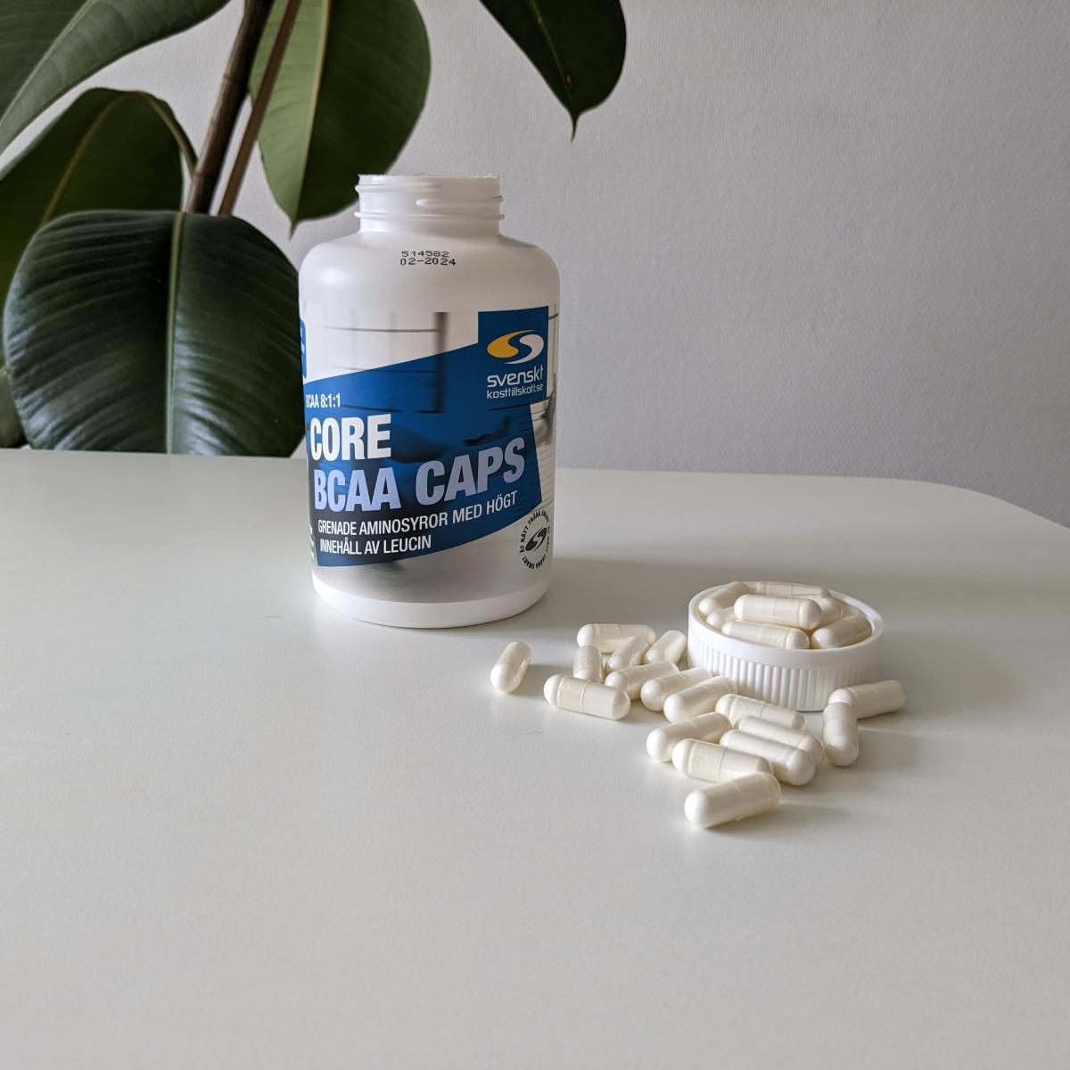 Core BCAA Caps burk och kapslar på vitt bord i dagsljus foto av oss under testet