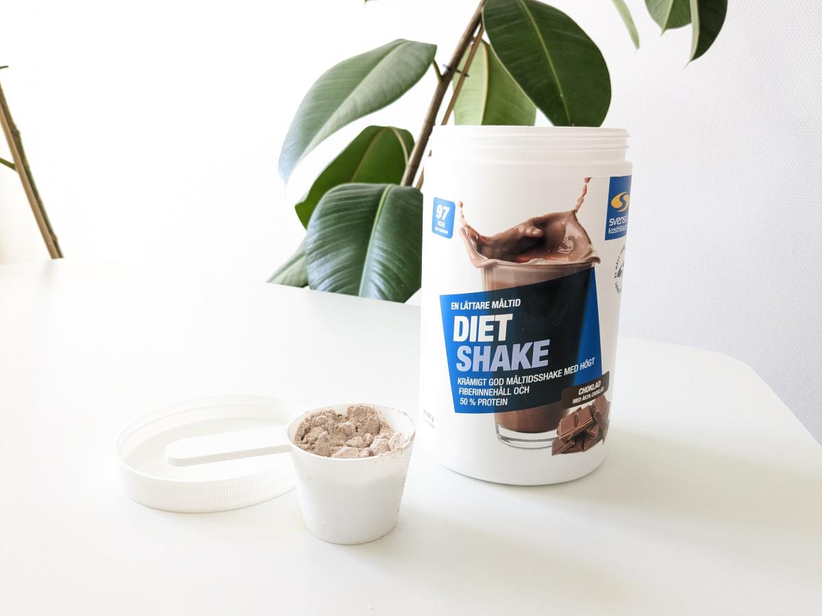 Diet Shake choklad med skopa på bord i dagsljus, fotad av oss under testet