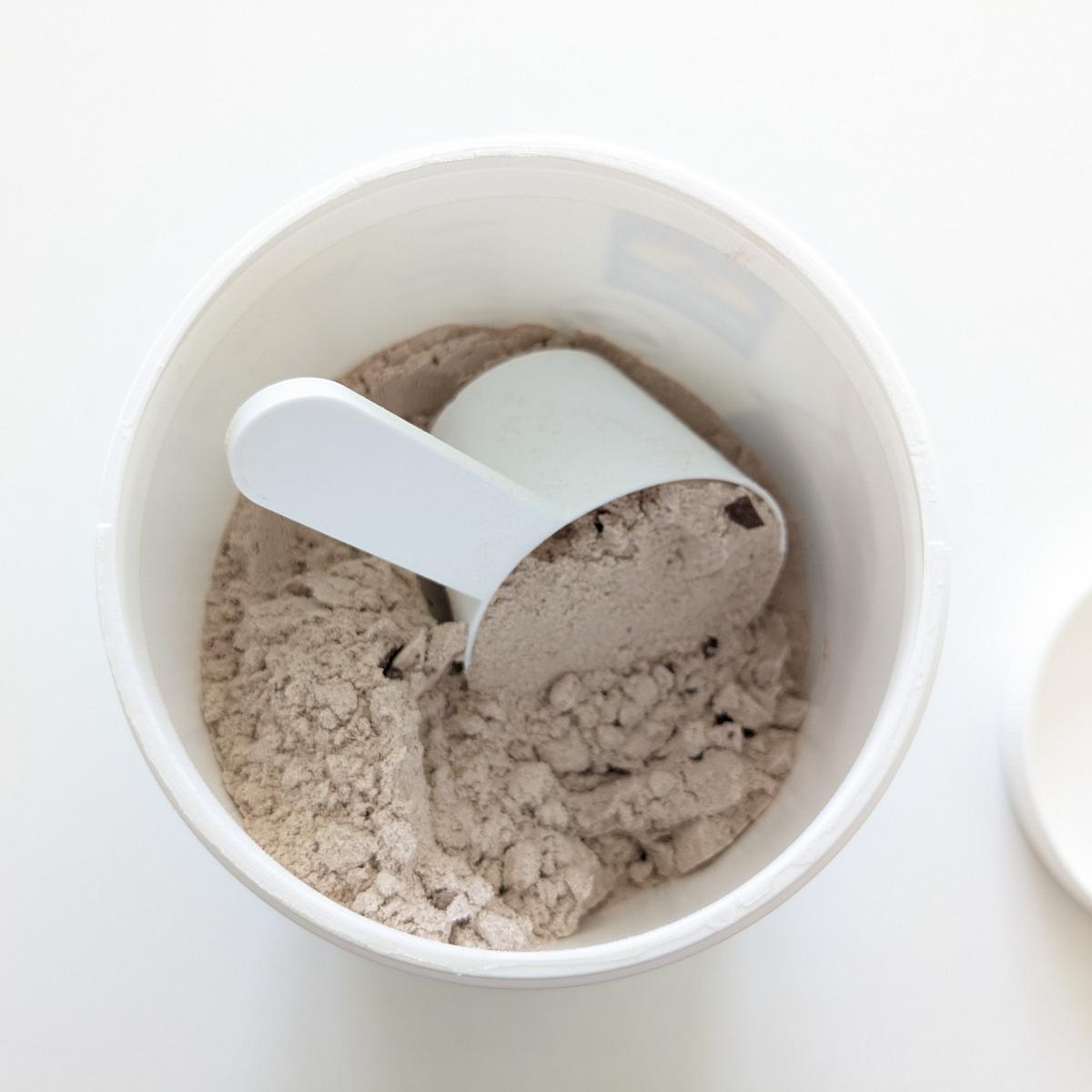 Öppen burk med Diet Shake choklad och skopa, chokladbitar syns i pulvret, fotad av oss under testet