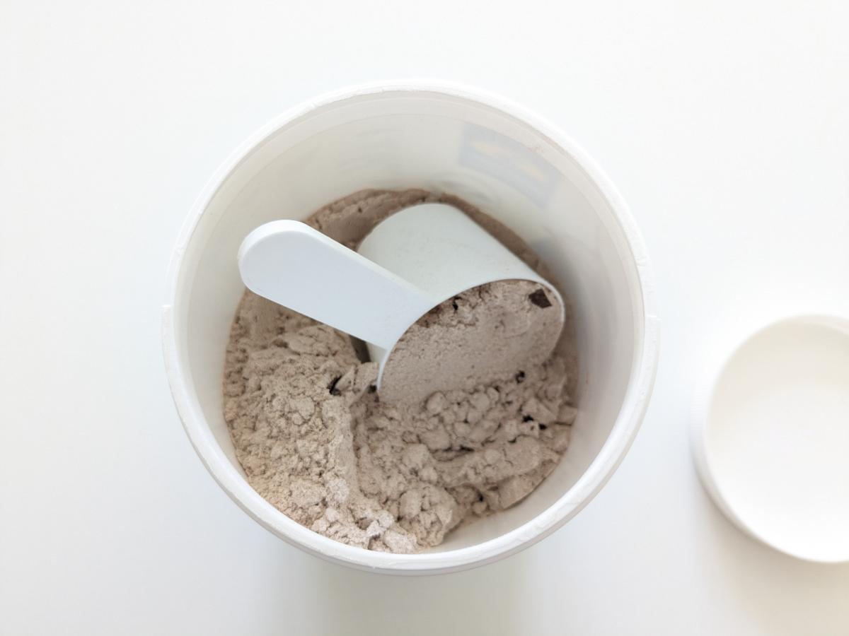 Öppen burk med Diet Shake choklad och skopa, chokladbitar syns i pulvret, fotad av oss under testet