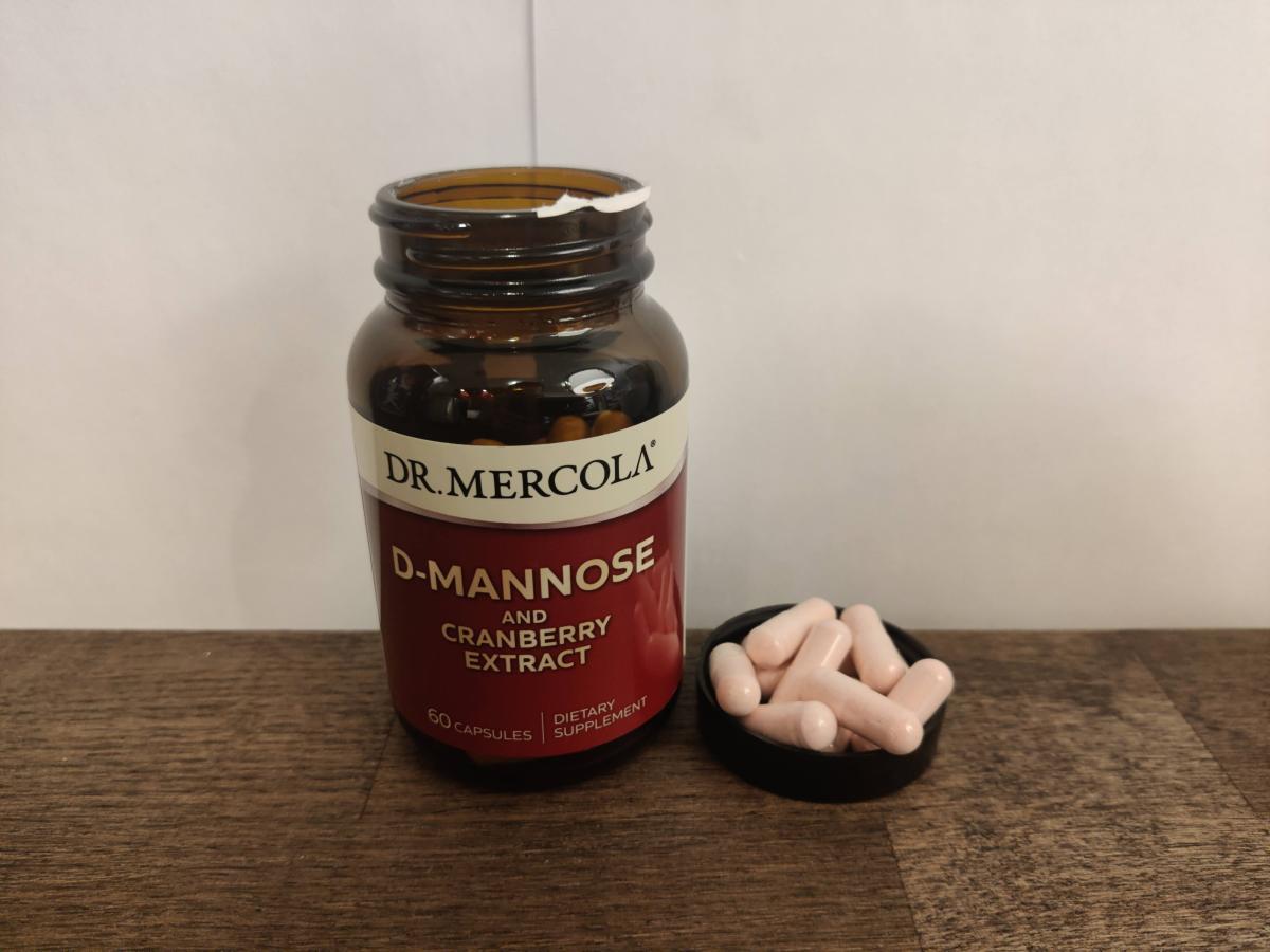 Dr Mercola D‑Mannose kapslar bredvid burken på träbord i mjukt dagsljus