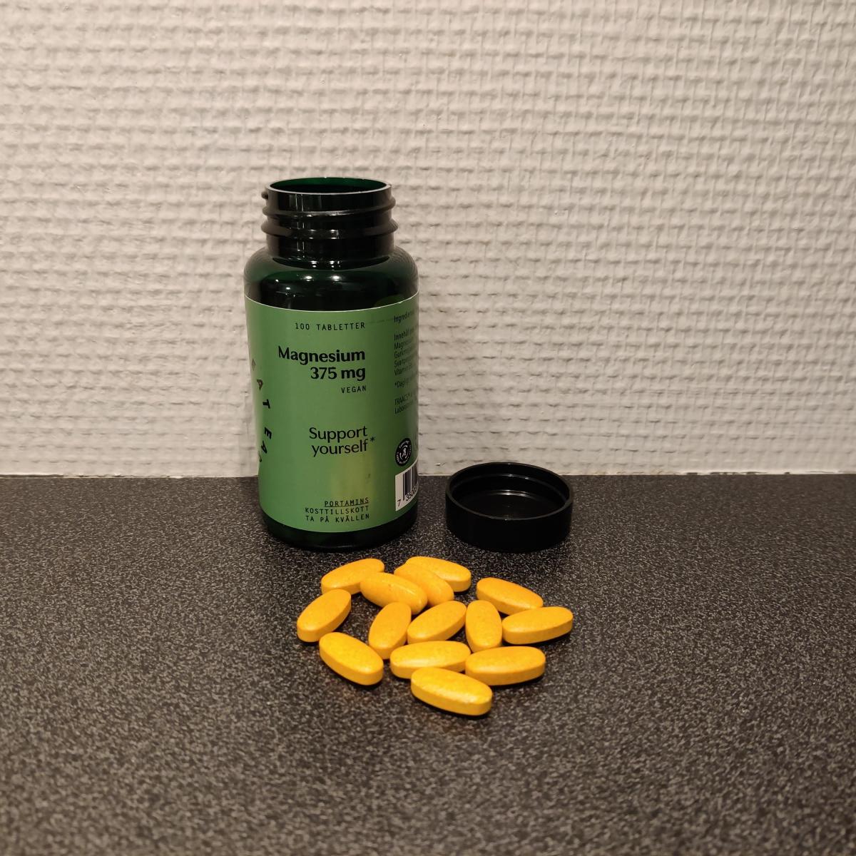 Burk med Great Earth Magnesium 375 mg och några tabletter bredvid, foto av oss