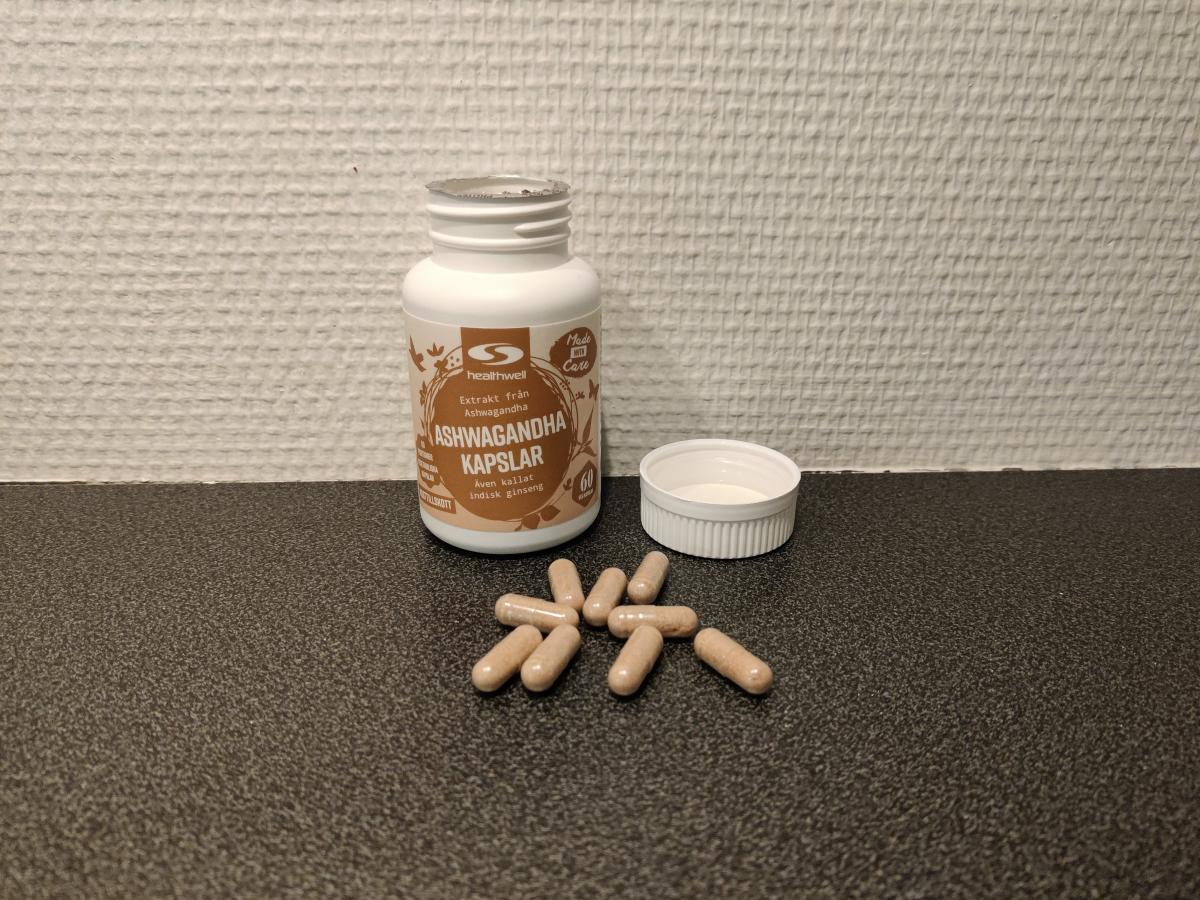 Healthwell Ashwagandha Extrakt och ljusbruna kapslar på bänkskiva, taget av oss under testet