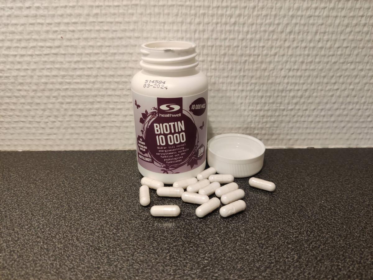 Healthwell Biotin 10 000 kapslar fotade av oss på mörk bänkskiva med öppnad burk