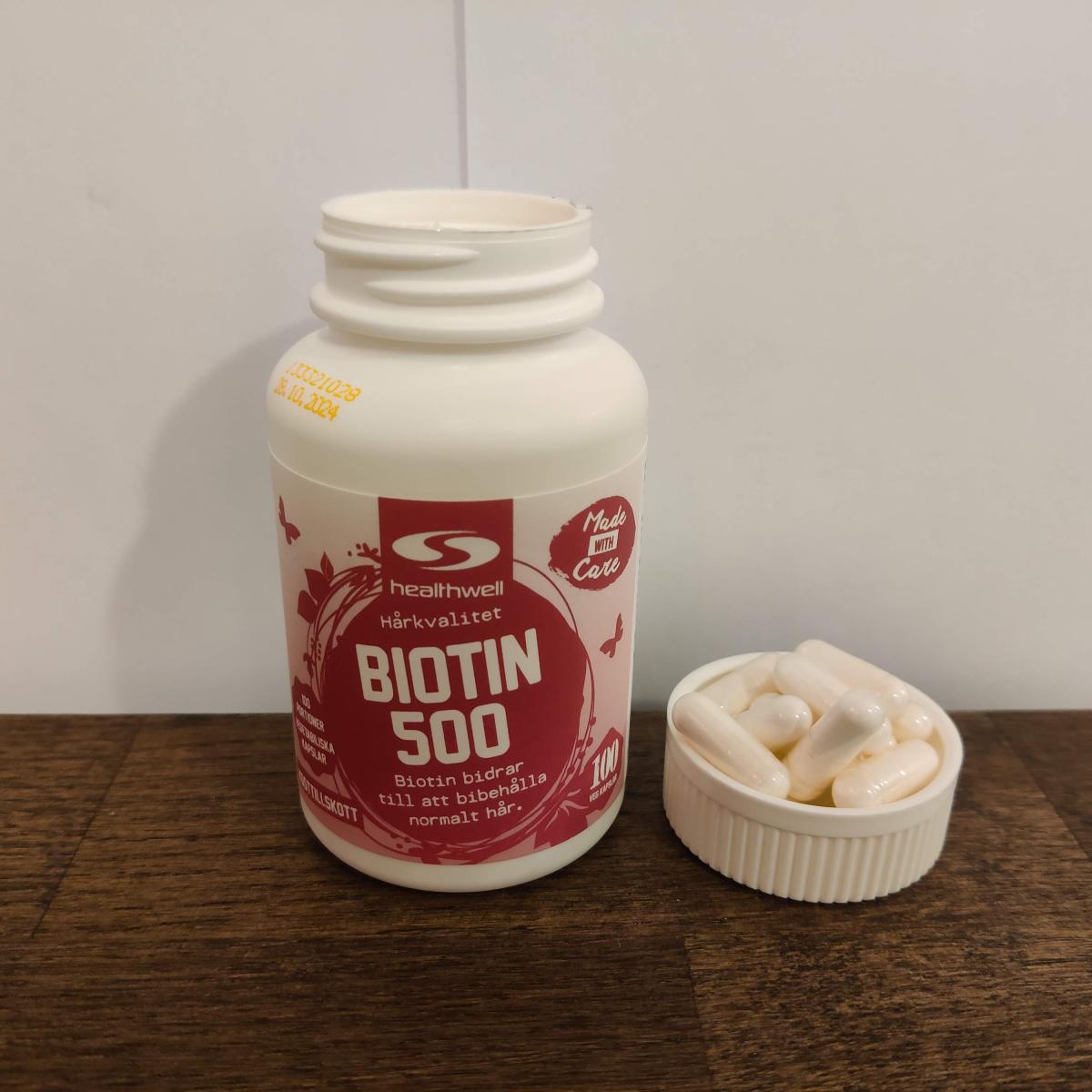 Healthwell Biotin 500 framifrån med kapslar intill, eget foto