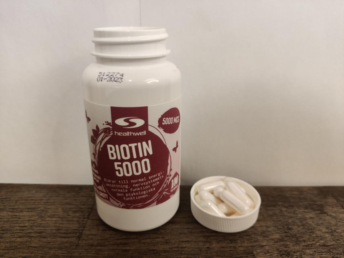 Healthwell Biotin 5000 på träbord med kapslar nära foto av oss