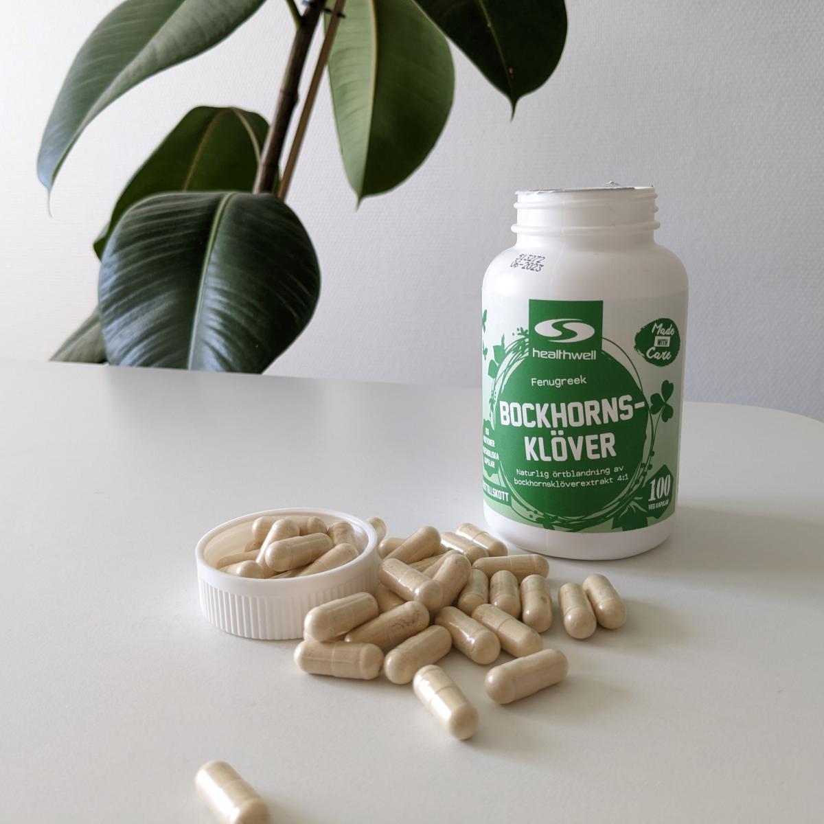 Vår egen bild av Healthwell Bockhornsklöver, burk och kapslar på bordet med grön växt i bakgrunden under testet