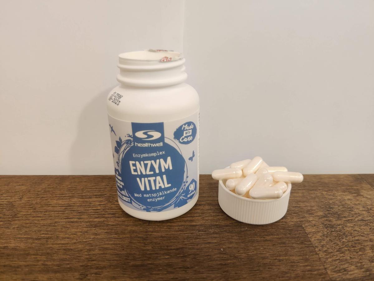 Healthwell Enzym Balans på träbord med kapslar bredvid, taget under test