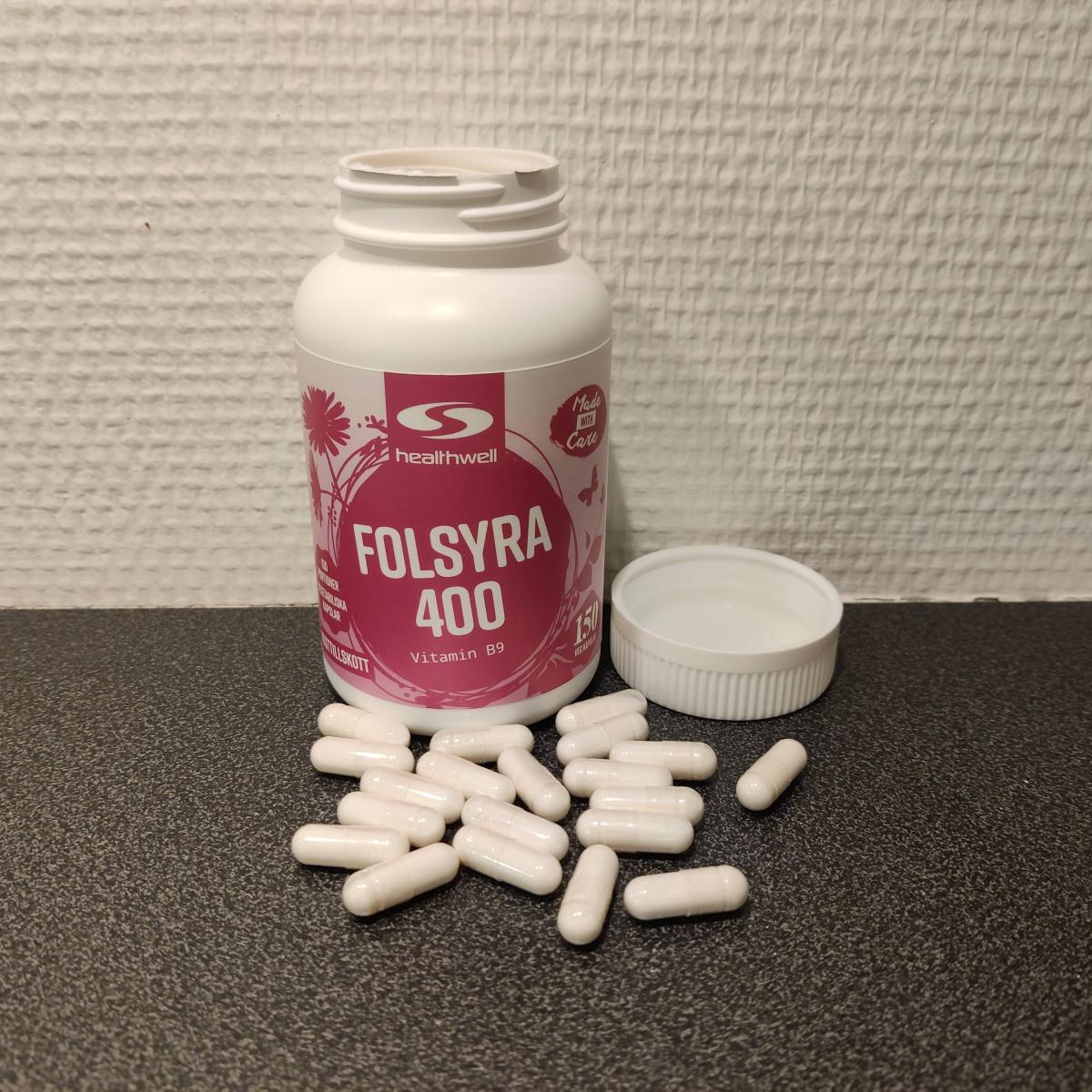 Healthwell Folsyra 400 med några kapslar placerade bredvid burken, fotograferad av oss