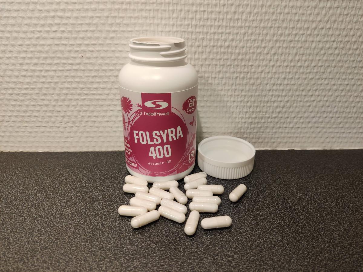 Öppen burk av Healthwell Folsyra 400 med kapslar utspridda på bänken, foto taget av oss under testet