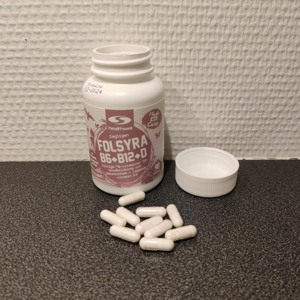 Healthwell Folsyra B6 B12 D på träbord bredvid kapslar, vårt eget foto
