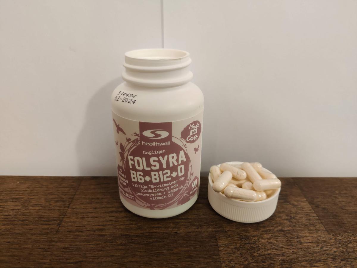Healthwell Folsyra B6 B12 D på träbord bredvid kapslar, vårt eget foto