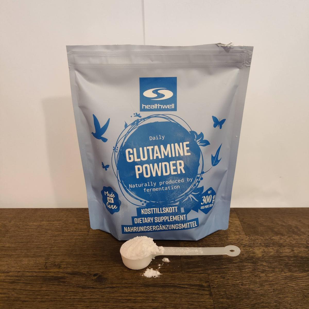 Healthwell Glutamine Powder med uppmätt skopa på trä, under vår testperiod