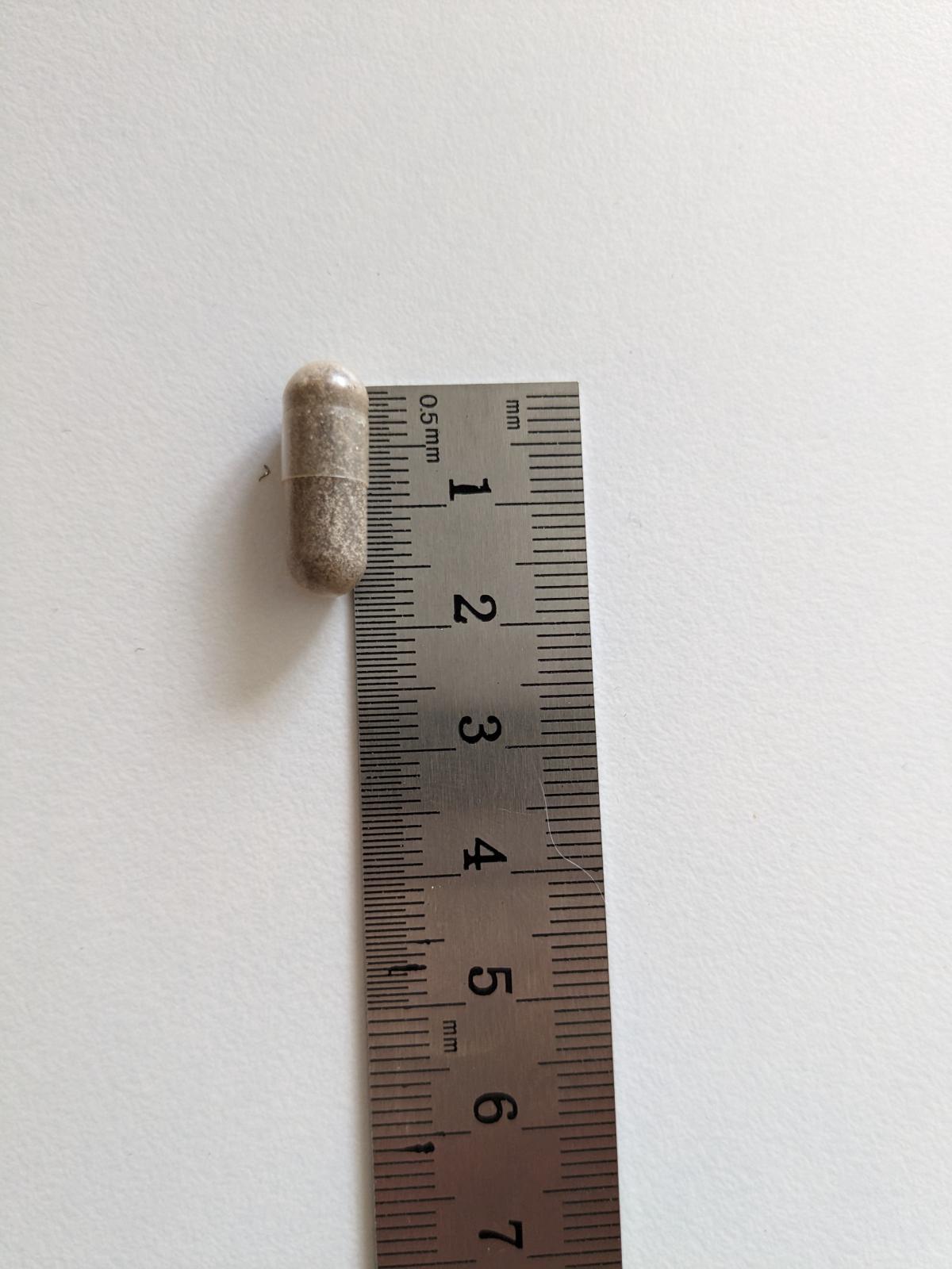 Kapsel från Healthwell Järn Skonsam bredvid linjal, ungefär 1,8 cm