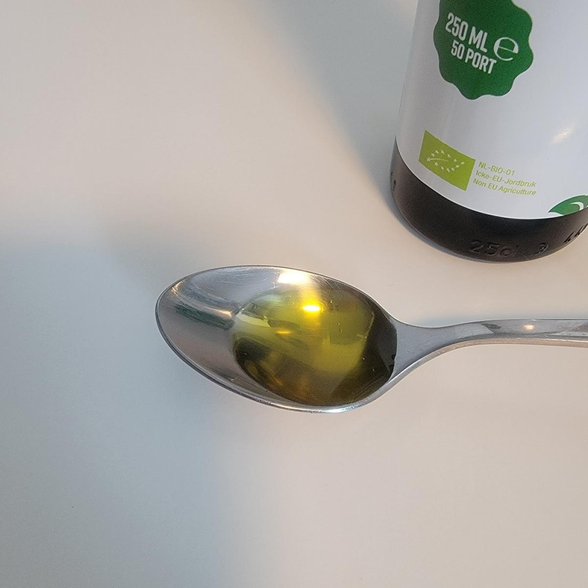 Tesked med klar, gyllene linfröolja från Healthwell framför flaskans etikett, foto av oss