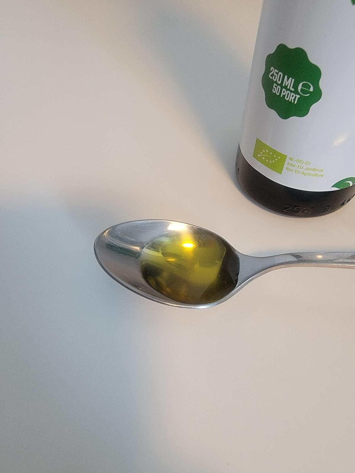 Tesked med klar, gyllene linfröolja från Healthwell framför flaskans etikett, foto av oss