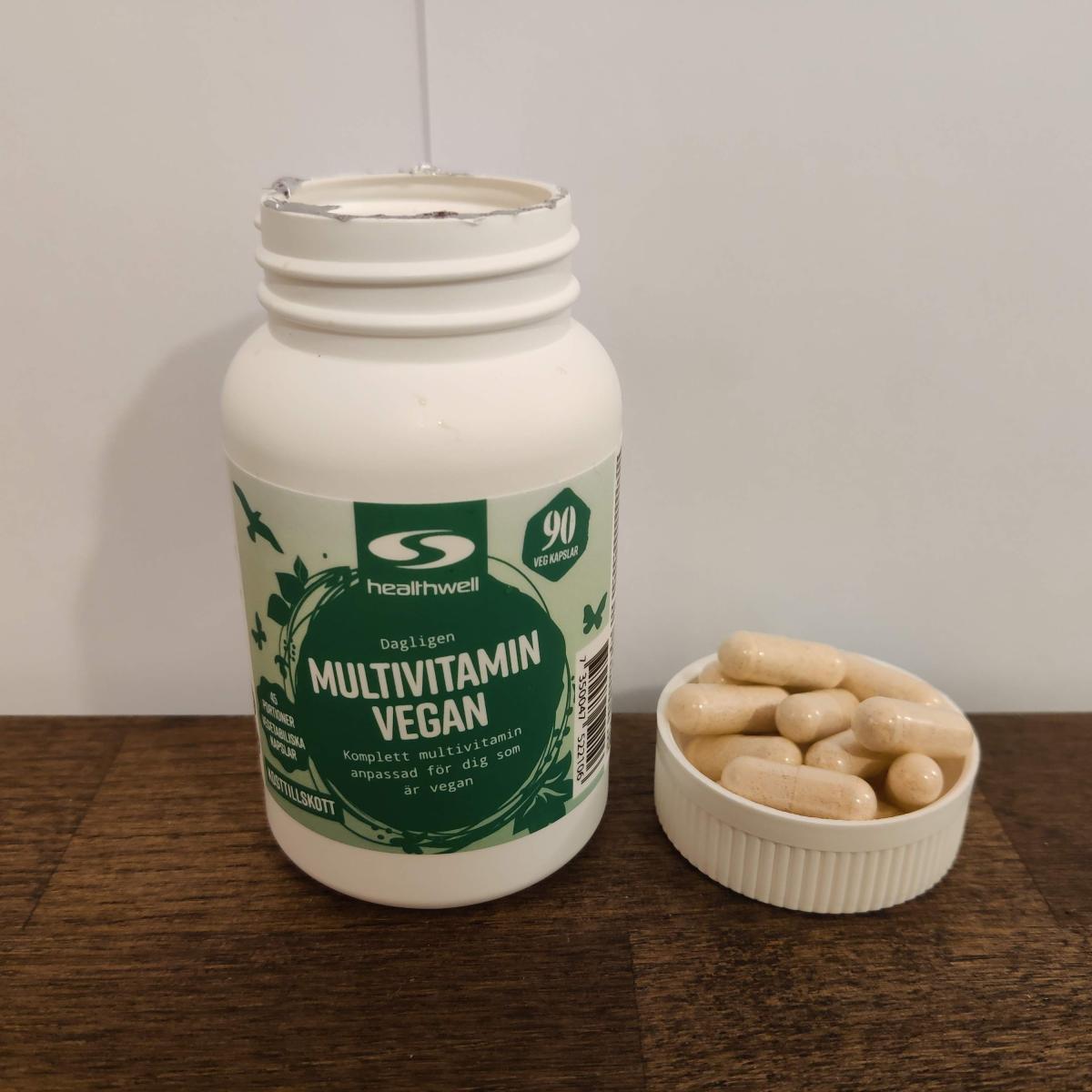 Närbild tagen av oss på Healthwell Multivitamin Vegan med kapslar i locket på ett träbord