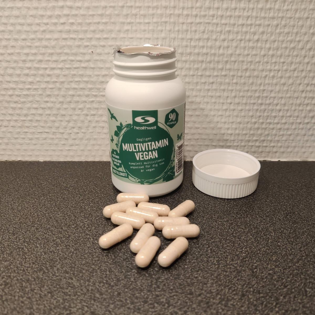 Healthwell Multivitamin Vegan fotograferad av oss – öppnad burk med ljusgula kapslar på bänken