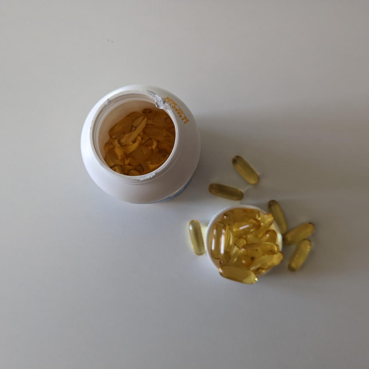 Öppnad burk av Healthwell Omega-3 Plus ovanifrån med några kapslar utspridda, eget testfoto