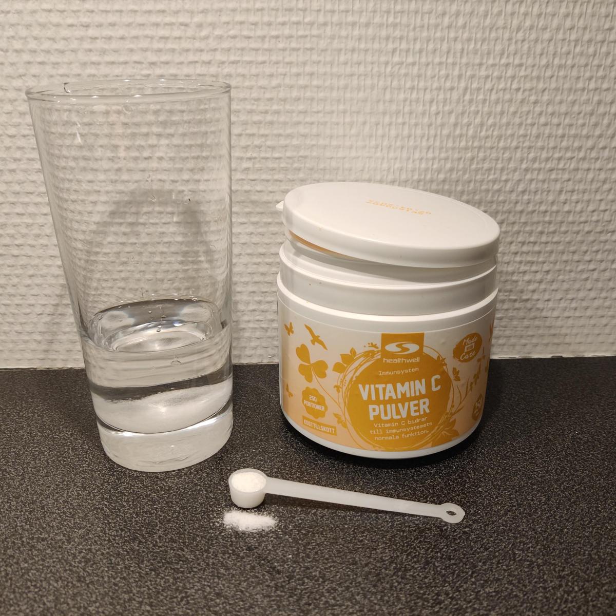 Närbild på Healthwell Vitamin C Pulver på sked framför burken, fotad av oss