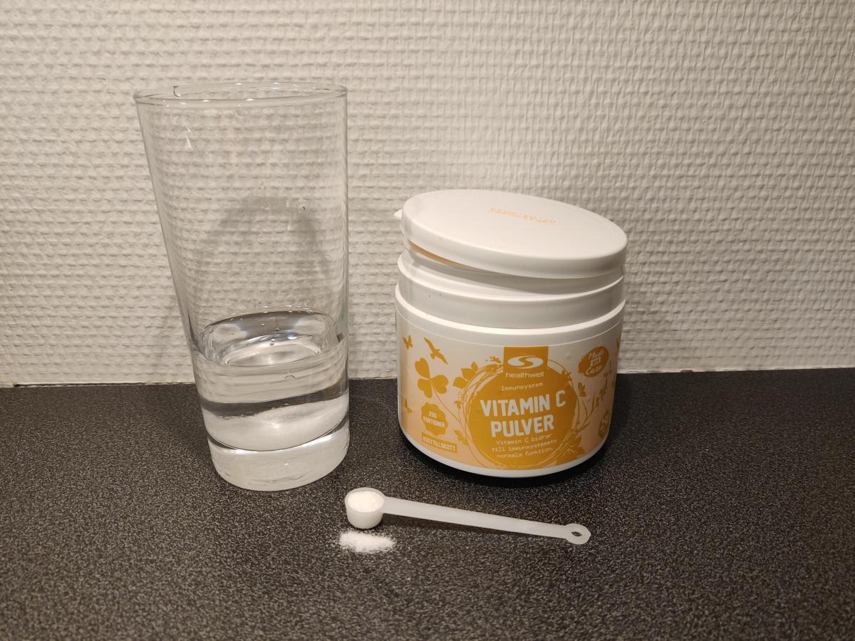 Healthwell Vitamin C Pulver med skopa och glas vatten, fotad av oss under testet