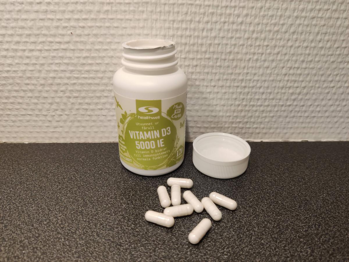 Healthwell Vitamin D3 5000 IE, öppnad burk med kapslar på mörk bänkskiva, foto från vårt test