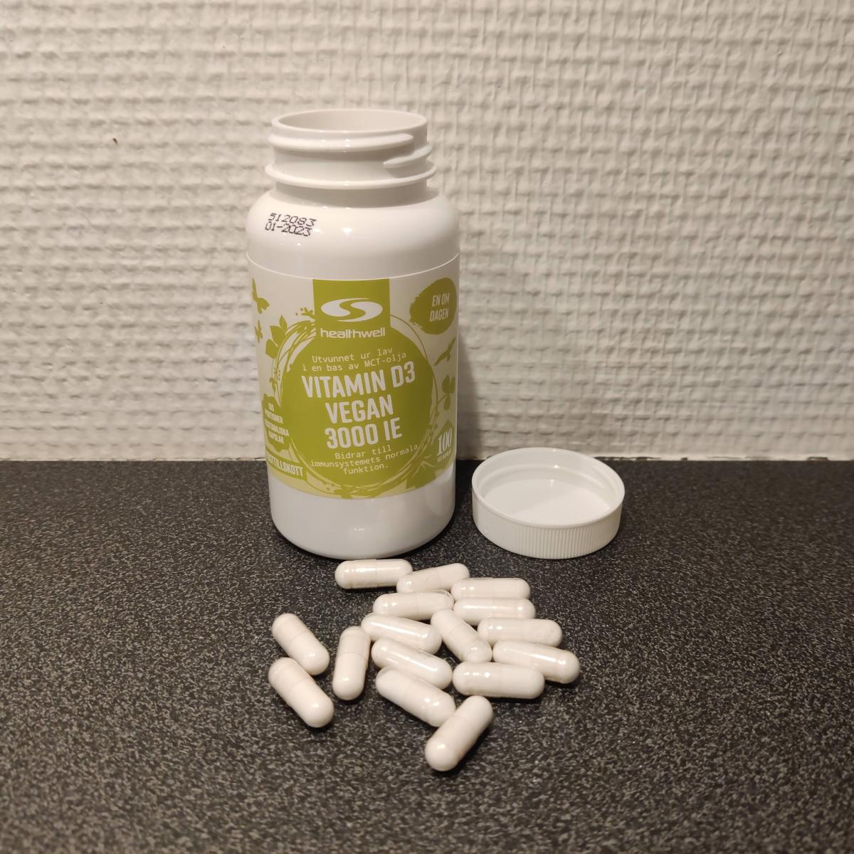 Healthwell Vitamin D3 Vegan på träbord med några kapslar bredvid, egen bild i naturligt ljus