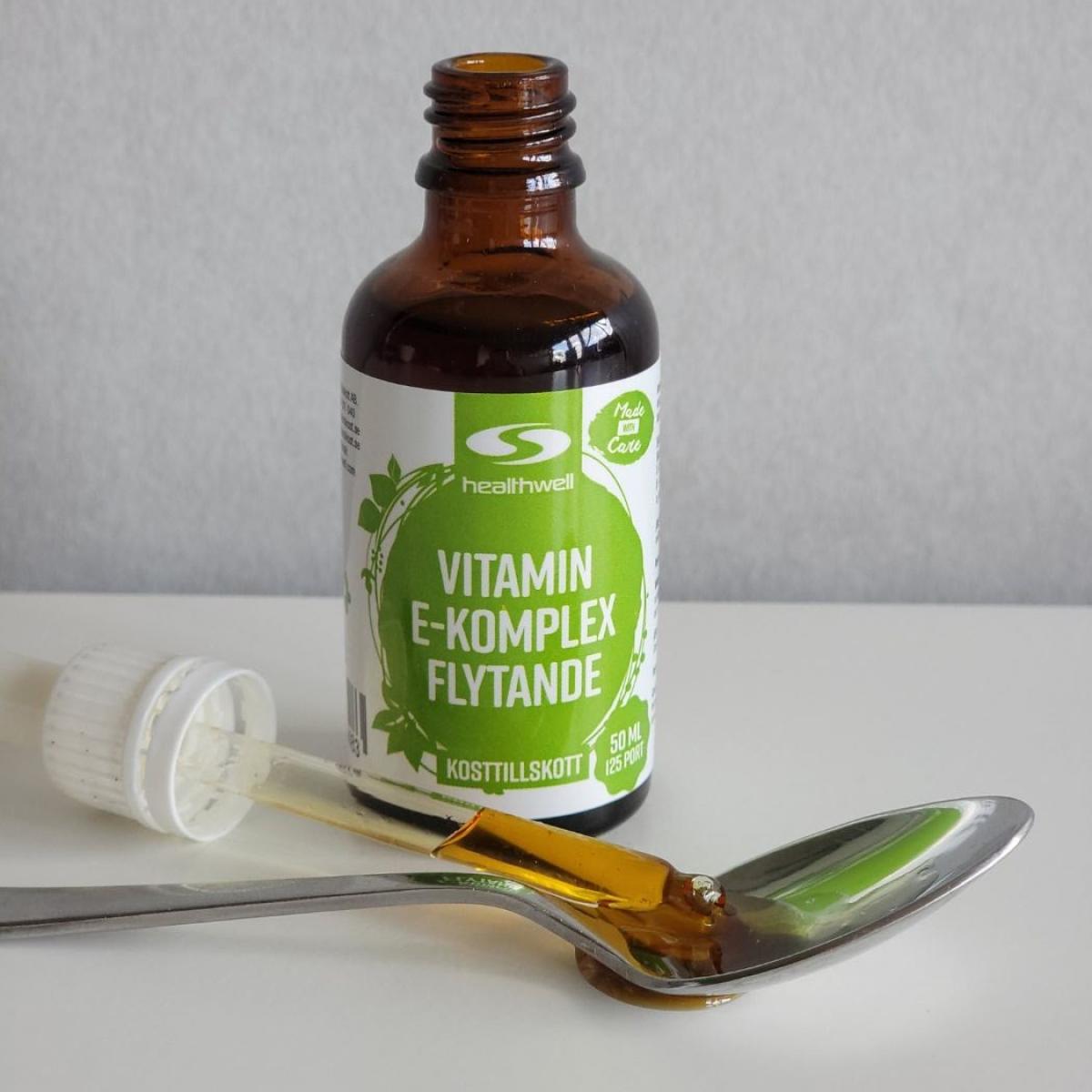 Närbild uppifrån av Healthwell Vitamin E Komplex där en seg droppe samlas i skeden under dosering