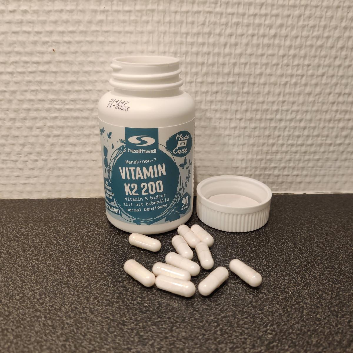 Healthwell Vitamin K2 på träbord, kapslar samlade intill locket, fotograferad av oss