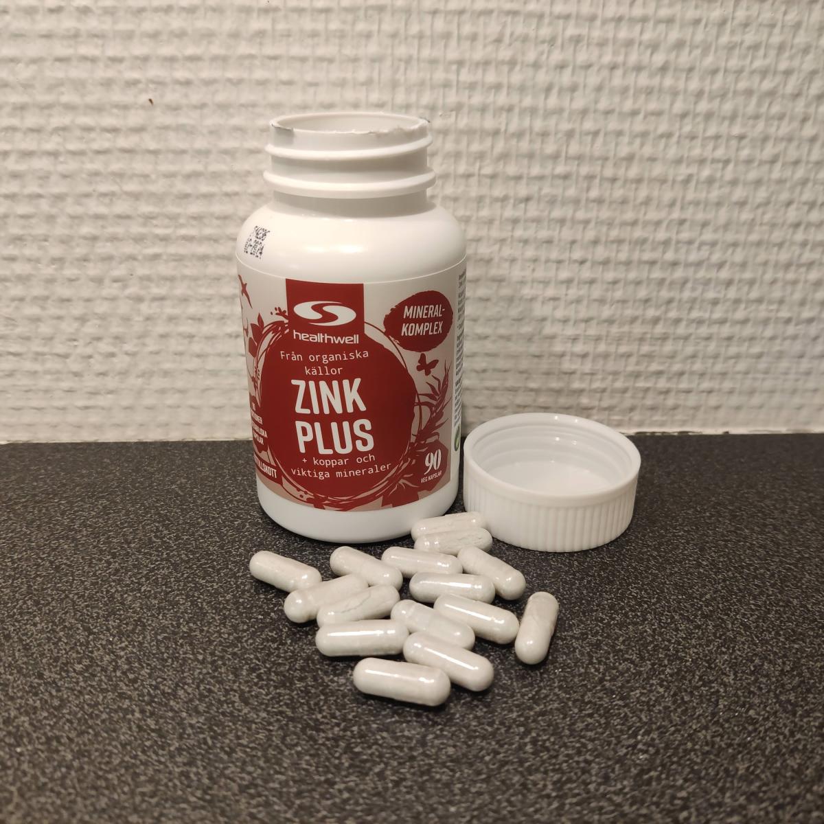 Närbild av Healthwell Zink 25 Plus på träbord med några kapslar i locket, tagen av oss