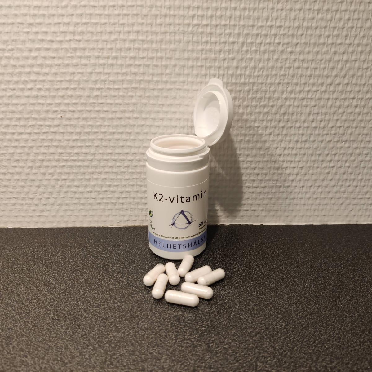 Helhetshälsa K2-Vitamin på träbord med fyra upplagda kapslar, fotograferad i hemmaljus